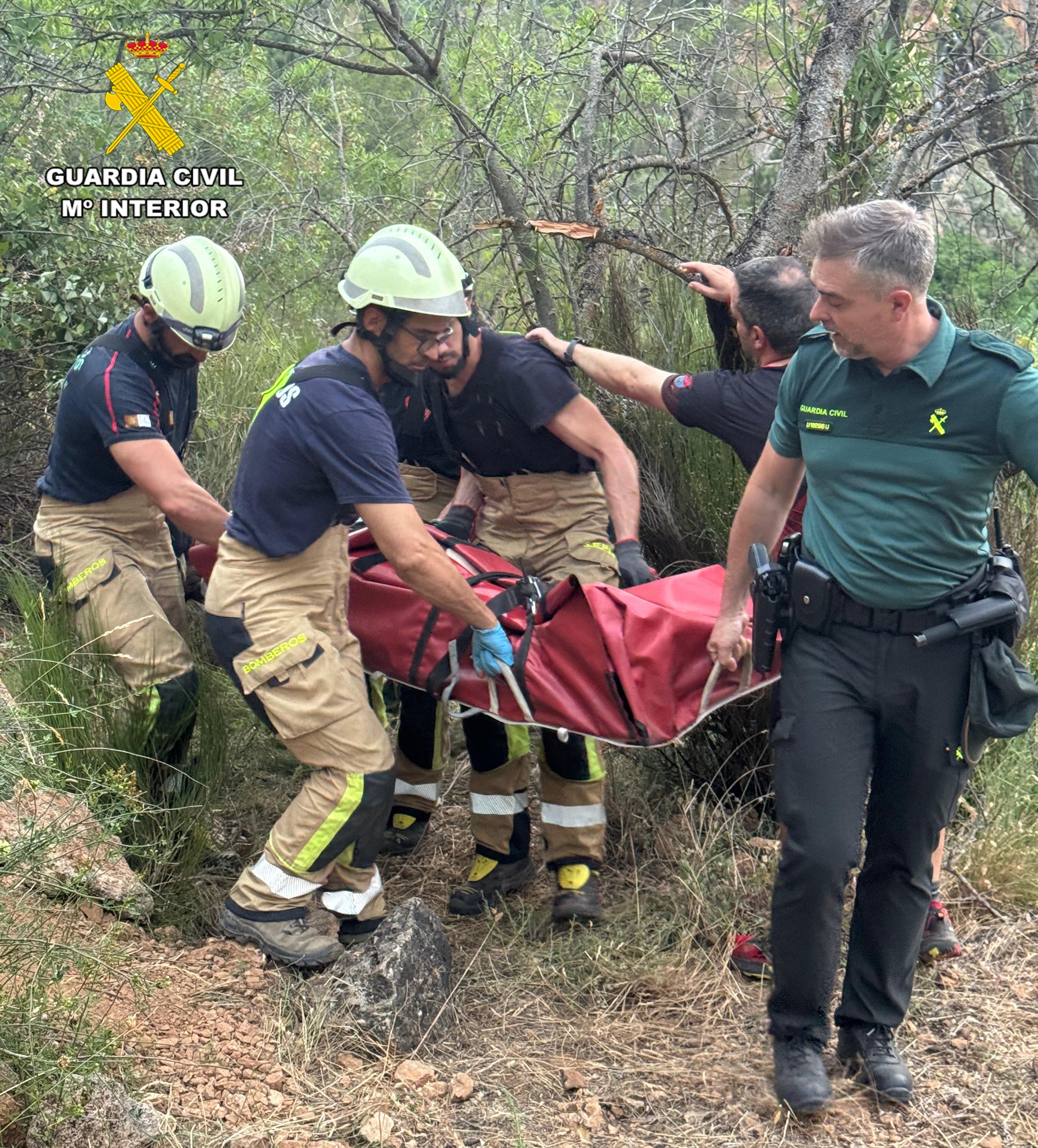 Equipo de rescate portando a la excursionista en camilla a través de un sendero estrecho.